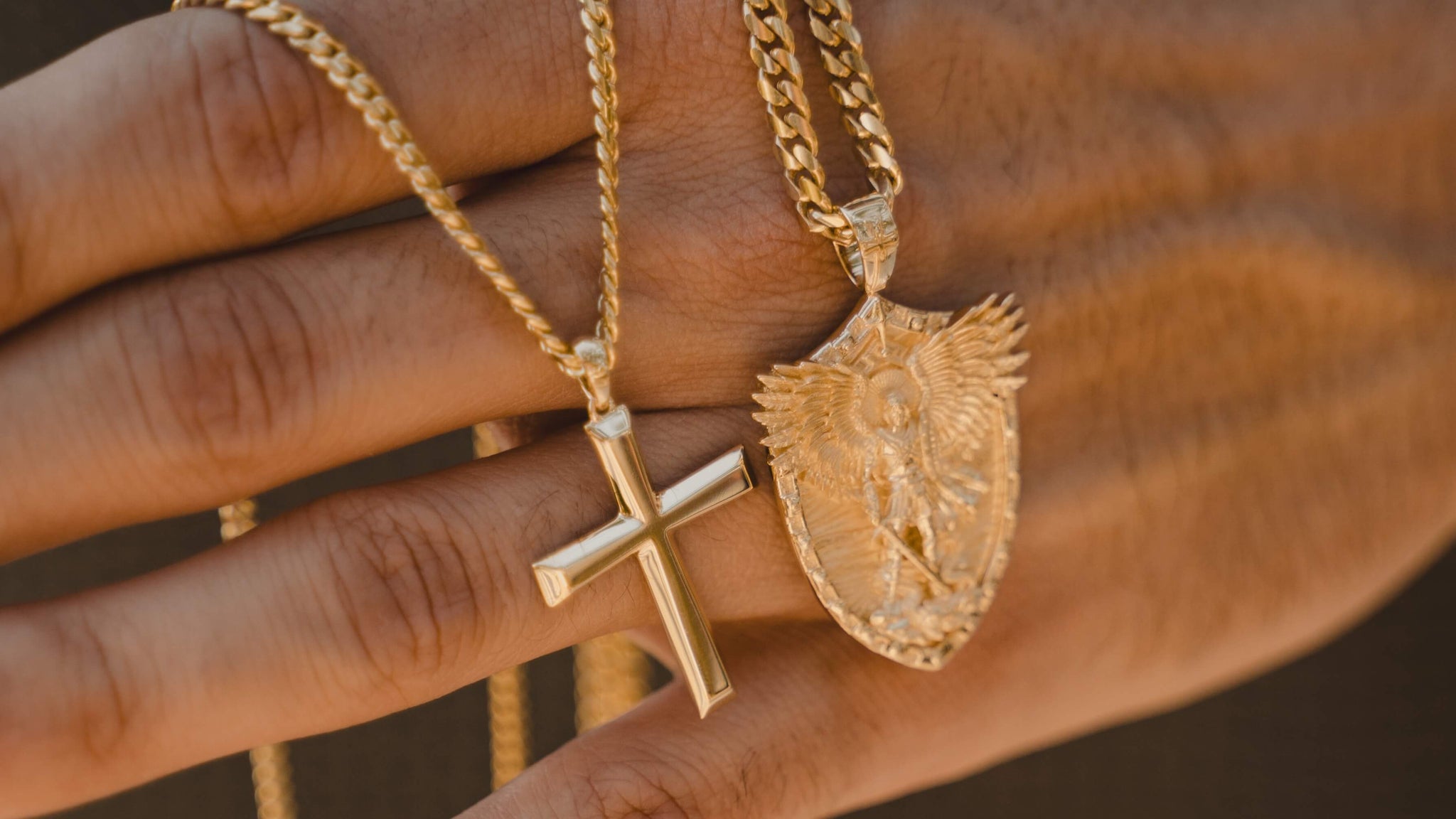 Man holding a solid gold cross pendant and gold Archangel shield pendant on Cuban link chains — best-selling gold pendants and charms from Liry's Jewelry