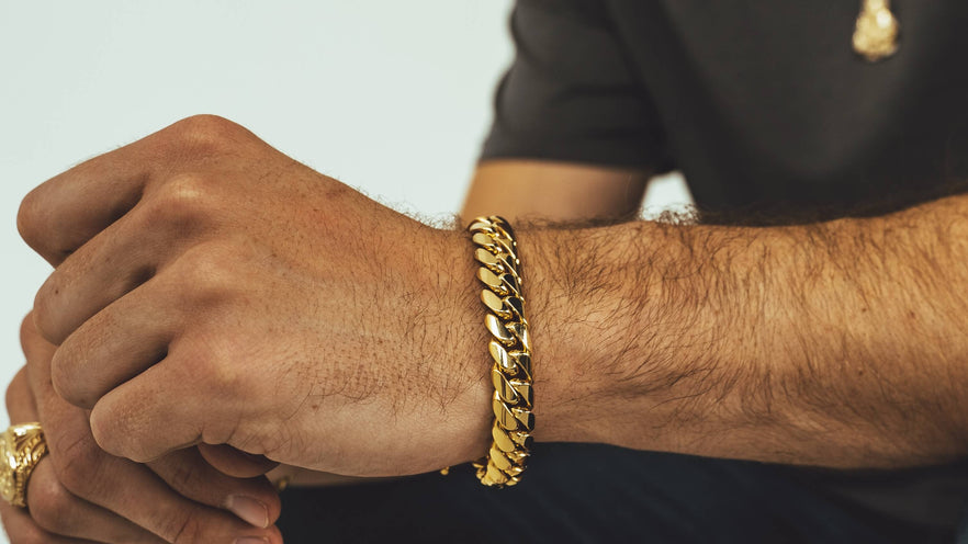 Man wearing a thick handmade solid gold Miami Cuban link bracelet with a gold ring and pendant — genuine 10kt, 14kt, and 18kt gold Cuban link bracelets from Liry's Jewelry