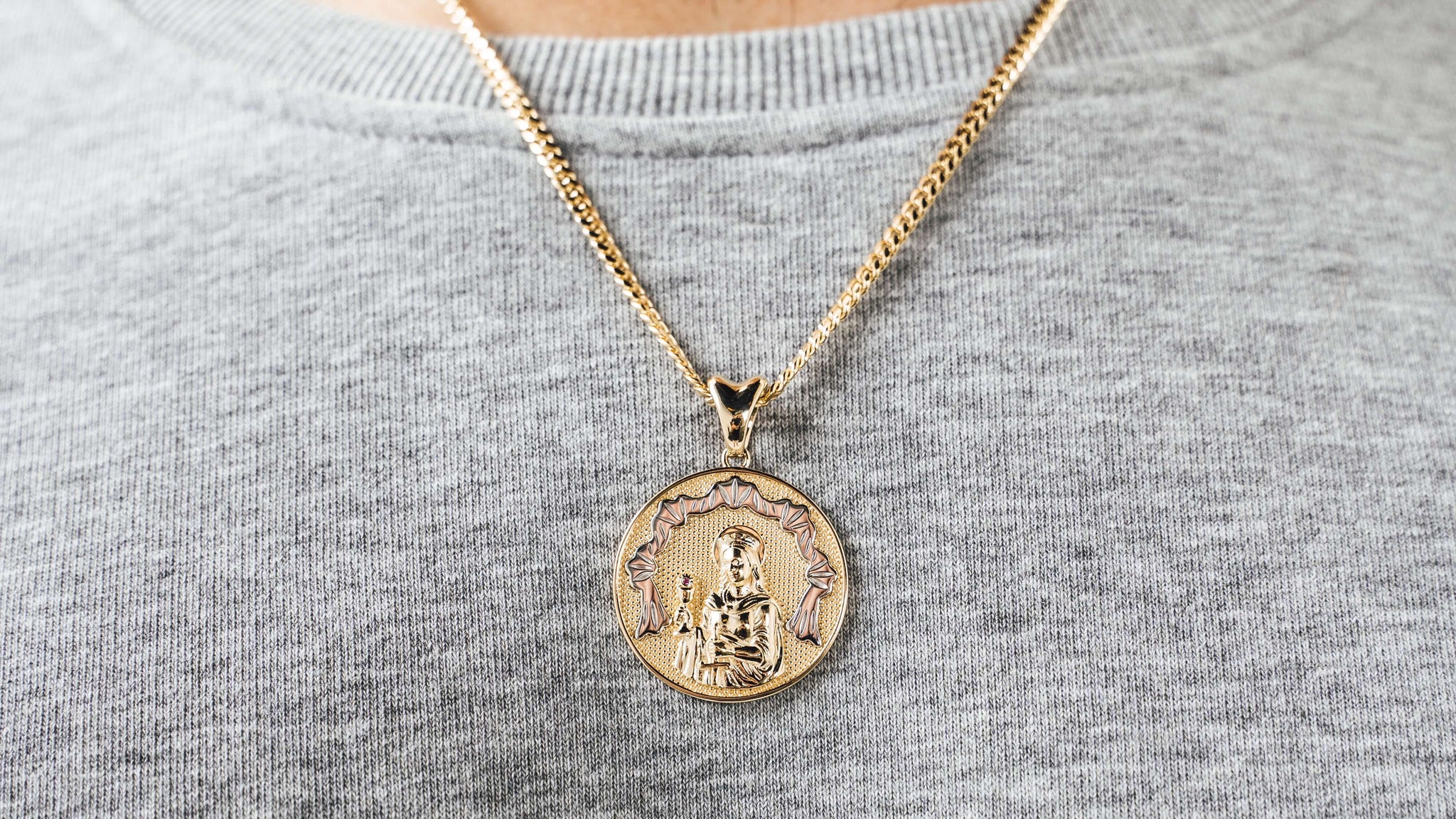 Solid gold Saint Barbara medallion pendant on a gold miami cuban link chain worn over a grey sweatshirt — religious gold pendants and charms from Liry's Jewelry