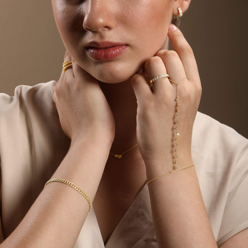 Close-up of a woman wearing gold jewelry including earrings, bracelet, and necklace against a brown background.